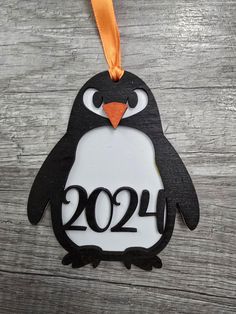 a black and white penguin ornament hanging on a wooden table with an orange ribbon