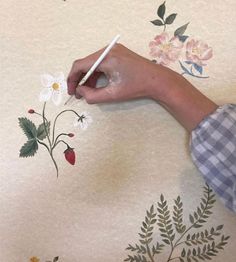 a person is painting flowers on a wall with white paint and a pencil in their hand