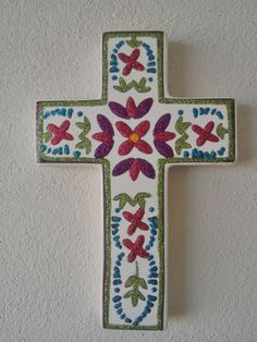 a cross with flowers painted on it is hanging from the side of a white wall