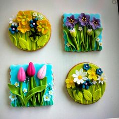 four decorated cookies sitting on top of a white table covered in icing and flowers