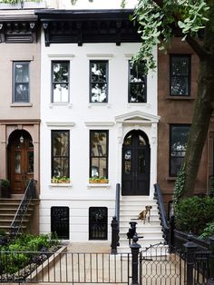 a white two story house with black doors and windows on the second floor, next to a wrought iron fence