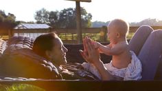 a woman holding a baby while sitting in a hammock with her hands together