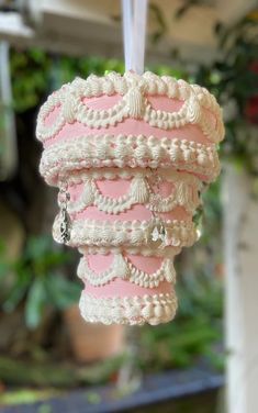 a pink and white ornament hanging from a string in front of some plants