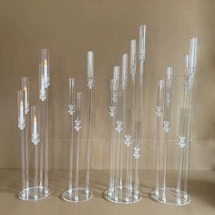 several clear glass candlesticks are lined up in a row on a table next to a wall