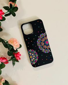 a black phone case with colorful flowers on it next to some pink and red roses