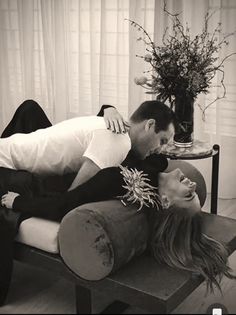 a man and woman laying on top of a couch next to a vase with flowers