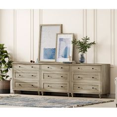 a dresser with two pictures on top and plants in the bottom, next to it