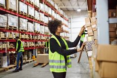 two people in yellow vests and safety vests are picking boxes from the shelves