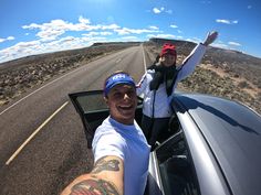 a man and woman taking a selfie in the back of a car on an open road