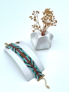 two bracelets and a vase with flowers in it on a white surface next to each other