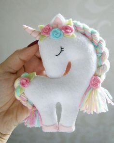 a hand holding a stuffed unicorn with flowers on it's head and manes