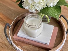 a jar of cream sitting on top of a wooden table next to a vase with white flowers