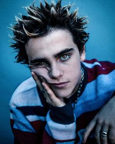 a young man with spiked hair and piercings posing for a photo in front of a blue background