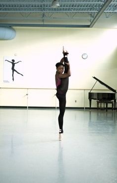 a woman in a dance studio with her arms up and one leg raised, while the other