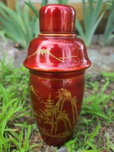 a red vase sitting in the grass with trees on it's lid and bottom