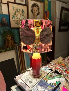 a table topped with a red candle next to a pile of paper and pictures on the wall