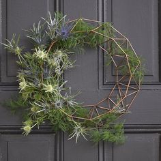 a wreath made out of branches and flowers hanging on a gray painted door with metal bars