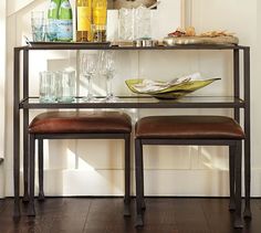 two brown leather stools sitting next to a table with bottles and glasses on it