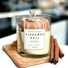 a cinnamon roll candle sitting on top of a wooden tray next to two cinnamon sticks