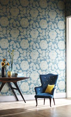 a blue chair sitting in front of a table with flowers on it and a vase