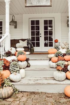 pumpkins and gourds sit on the front steps of a white house with porch railing