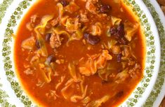 a white bowl filled with pasta and meat soup on top of a green and white plate