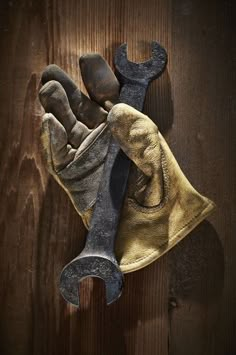 an old pair of work gloves hanging on a wooden wall next to a wrench