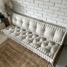 a white couch sitting on top of a rug next to a brick wall and potted plant