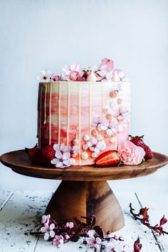 a strawberry cake with white frosting and fresh strawberries is on a wooden platter