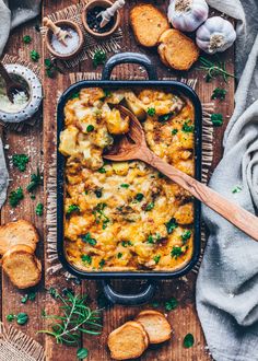 a casserole dish with cheese and bread on a wooden table next to garlic