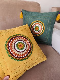 two decorative pillows on a couch with one being embroidered onto the pillow and the other is handmade