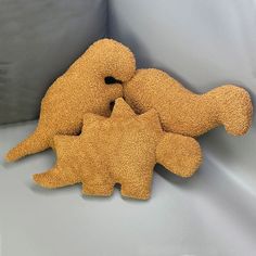 three stuffed animals sitting next to each other on a white cloth covered surface, one is yellow and the other is brown