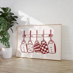 an art print with kitchen utensils hanging on a clothes line in front of a potted plant