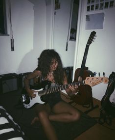 a woman sitting on the floor playing an electric guitar with two other guitars behind her