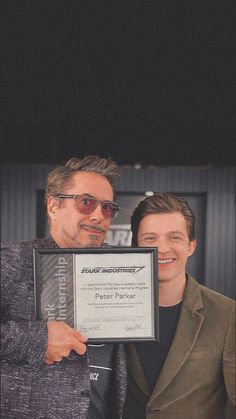 two men standing next to each other holding an award plaque in front of their faces