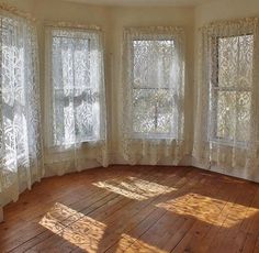 an empty room with three large windows and wooden floors in the center is covered by white lace curtains