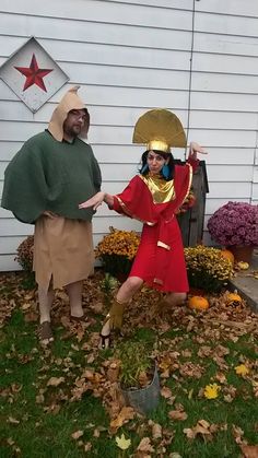 two people dressed up in costumes posing for the camera outside their house, one is holding an umbrella and the other is wearing a costume