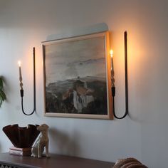 a painting hanging on the wall next to two candles and a dog figurine