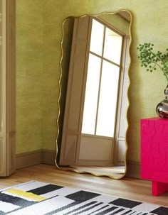 a large mirror sitting on top of a wooden floor next to a pink cabinet and vase