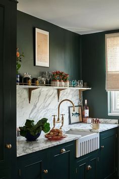 a kitchen with green walls and marble counter tops, brass faucet, sink, and window