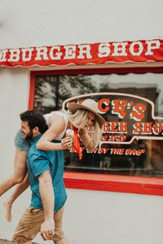 a man carrying a woman on his back while walking past a burger shop with a sign that says it's hell show