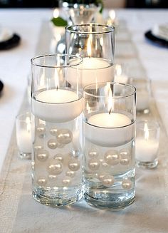 candles are lit on a table with clear glass vases filled with water and pearls