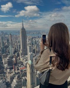 a woman taking a photo with her cell phone on top of the empire building in new york city