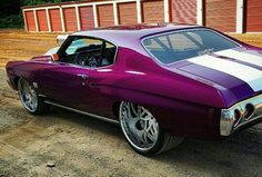 a purple and white car parked on top of a dirt road next to a building