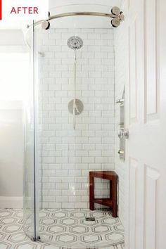 a white tiled bathroom with a stand up shower and wooden side table in the corner