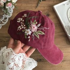 a red hat with flowers on it sitting on top of a table next to lace