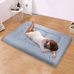 a woman laying on top of a blue mattress in the middle of a wooden floor