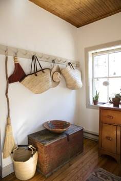 an old trunk is sitting on the floor in front of a window with hanging baskets and brooms