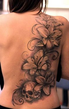 a woman's back with flowers and a skull tattoo on her left side ribcage