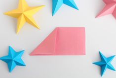 three origami stars and one folded paper star on a white surface with pink, blue, and yellow colors